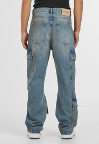 Jeans cargo din denim de culoare albastră deschisă, cu o croială lejeră, multiple buzunare laterale și o etichetă din piele pe talie, în partea din spate.