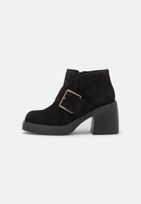Bottines en daim noir avec un bout carré, dotées d'une large bride et d'une boucle dorée. Talon épais noir offrant stabilité.