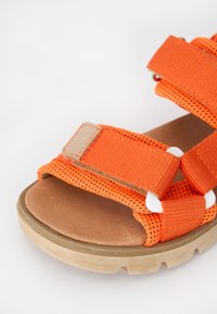 Orange sandaler med remdesign, som har ett ventilerande tyg, syntetisk sula och en texturerad tan inläggssula. Vita detaljer på remmarna.