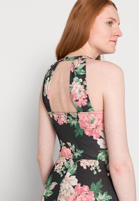 Vestido floral com fundo preto, apresentando flores rosa e verdes, um design de costas em forma de chave e sem mangas. Textura de tecido suave.