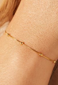 Gold bracelet featuring a delicate chain with alternating spherical accents, resting on textured skin, showcasing a slim design.