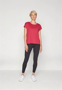 Rød t-shirt med korte ærmer kombineret med sorte leggings, der har et let stof og en afslappet pasform, fremhævet af enkle designelementer.