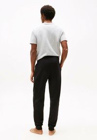 Camiseta gris de manga corta y pantalones de chándal negros ajustados. Material de algodón, corte relajado y cinturilla elástica con puños acanalados.