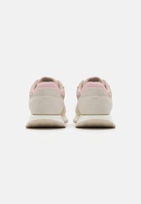 Zapatillas atléticas rosadas y beige con parte superior de ante y malla, tacón redondeado y suela de goma texturizada, que presentan un diseño minimalista.