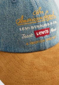 Blå denim og brun semsket baseballcap med brodert Levi's-merke og tekst som inkluderer "American Legend" og "A Tradition Since 1873."