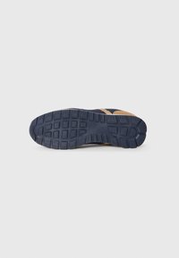 Shoe sole in dark blue rubber with textured grip pattern; features light tan edging and rectangular indentations for traction.