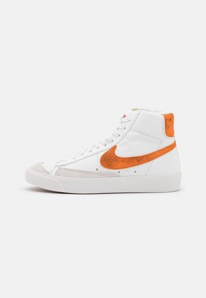 Hoge sneakers met een bovenwerk van wit leer, een oranje suède swoosh, een grijze suède neuskap en een witte rubberen zool. Ronde veters en een gevoerde kraag.