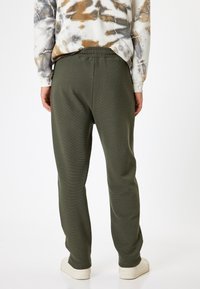 Groene, getextureerde joggers met een relaxte pasvorm, voorzien van een elastische tailleband en boorden. Gecombineerd met een tie-dye langemouwen top.