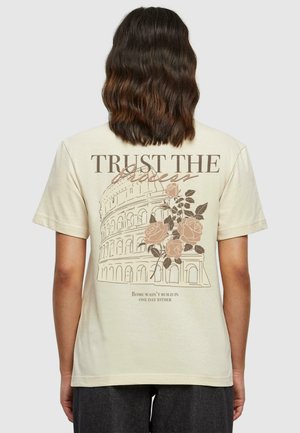 Beige cotton t-shirt featuring a graphic of the Colosseum, pink roses, and the text "Trust the Process" with an inspirational quote below.