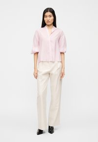 Ροζ πουκάμισο με κοντά μανίκια, V-λαιμόκοψη και λεπτομέρεια με κουμπιά, συνδυασμένο με μπεζ παντελόνια ψηλής μέσης και μαύρα μποτάκια αστραγάλου. Λείο υλικό.