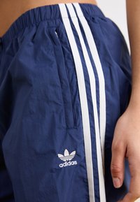 Tumed sinised kerged lühikesed püksid elastse vöökohaga, millel on valged triibud ja brodüüritud Adidas'i logo küljel.