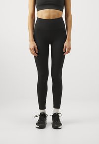 Svarta leggings med hög midja, gjorda av ett ribbat tyg, kombinerade med svarta träningsskor och vita strumpor. Slät textur, figurnära design.