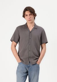 Chemise grise à manches courtes avec un col camp, texture lisse et détails de couture subtils, assortie à un jean en denim bleu.