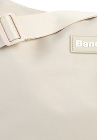 Beige stoffen schoudertas met een geribbelde textuur, voorzien van een verstelbare strap en een rechthoekig etiket met de opdruk "Bend."