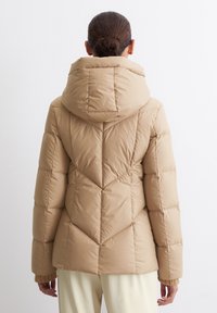 Wattierte Jacke in hellbeige mit gestepptem Chevron-Muster. Verfügt über eine Kapuze und gerippte Bündchen und besteht aus einem glatten, glänzenden Material.
