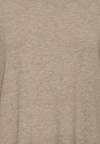 Gros plan d’un tissu tricoté uni marron clair avec un détail de fines côtes au bord inférieur.