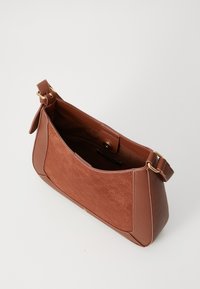 Bolso de hombro marrón con panel frontal texturizado, herrajes dorados, correa ajustable y parte superior abierta que muestra un bolsillo con cremallera en el interior y cierre a presión.