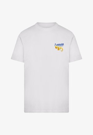 T-shirt bianca a girocollo con piccolo testo blu "Lemon Soda" e grafica di scorza di limone gialla sul petto a sinistra.