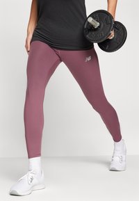 Fialové sportovní legíny s těsným střihem, s logem New Balance, v kombinaci s černými činkami a bílými sportovními botami.