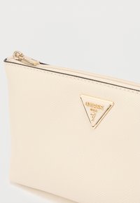 Μπεζ υφασμάτινη θήκη με υφή και πάνω φερμουάρ, διακοσμημένη με χρυσό τριγωνικό λογότυπο. Ομαλή επιφάνεια, συμπαγές σχήμα.