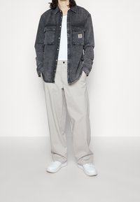 Tmavě šedá džínová košile se dvěma náprsními kapsami, nošená přes bílý top s ramínky, spárovaná se světlými šedými širokými kalhotami a bílými teniskami.