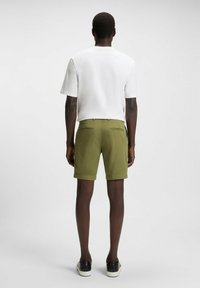 White short-sleeve t-shirt paired with olive green shorts. Shorts feature two back pockets and a smooth fabric texture. Black shoes complete the look.