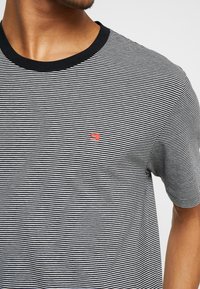 Stribet T-shirt med sorte og hvide vandrette striber, en sort rund hals og et lille rødt logo på venstre bryst.