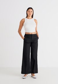 Black pinstriped wide-leg trousers with front pockets, paired with a white fitted tank top and silver flats. Smooth fabric texture, tailored fit.