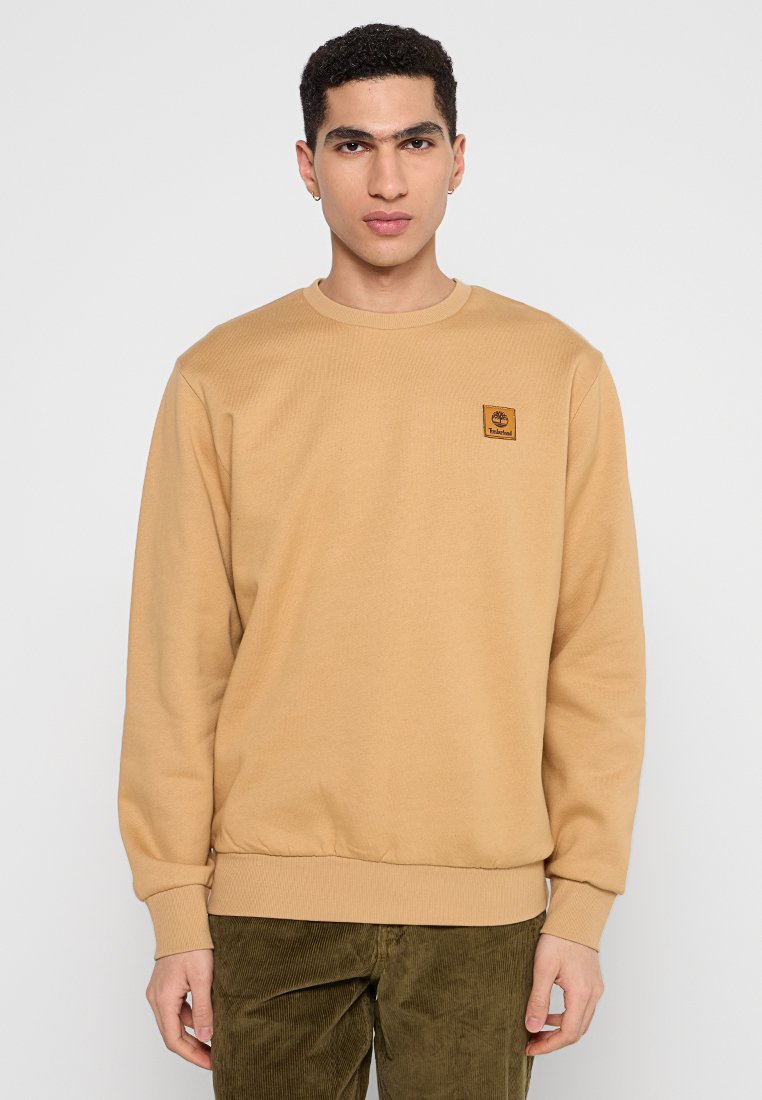 Felpa beige a girocollo con polsini e orlo ribattuti, caratterizzata da una piccola patch logo sul petto. Tessuto morbido con una trama liscia.