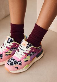 Baskets multicolores avec un motif léopard, des accents rose pastel, violet et orange, une semelle texturée et des lacets blancs.