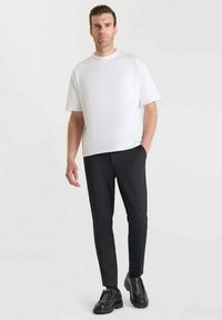 Witte, kortemouw t-shirt gecombineerd met zwarte, gestructureerde broek en zwarte schoenen. De outfit heeft een relaxte pasvorm en een minimalistisch ontwerp.