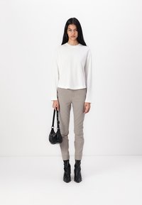 Fehér, hosszú ujjú felső, kockás, szűk nadrág, fekete bokacsizma és egy kis fekete kézitáska. Minimalista design, sima szövettextúra.