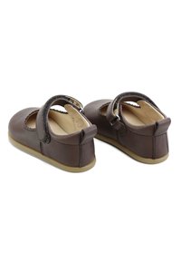 Zapatos Mary Jane de cuero marrón con puntera redondeada, correa ajustable y suela de goma color canela; presentan detalles cosidos y un forro interior suave.