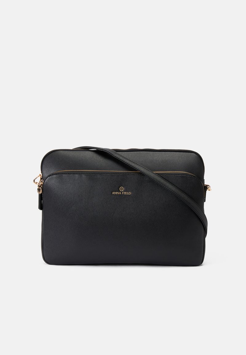 Schwarze synthetische Crossbody-Tasche mit glatter Textur, goldenen Reißverschlussakzenten und einem Logo auf der Vorderseite. Mit verstellbarem Riemen.