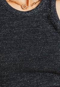 Débardeur noir à côtes avec un léger éclat. Présente un col rond et une texture visible. Accentué par un collier en chaîne circulaire dorée.