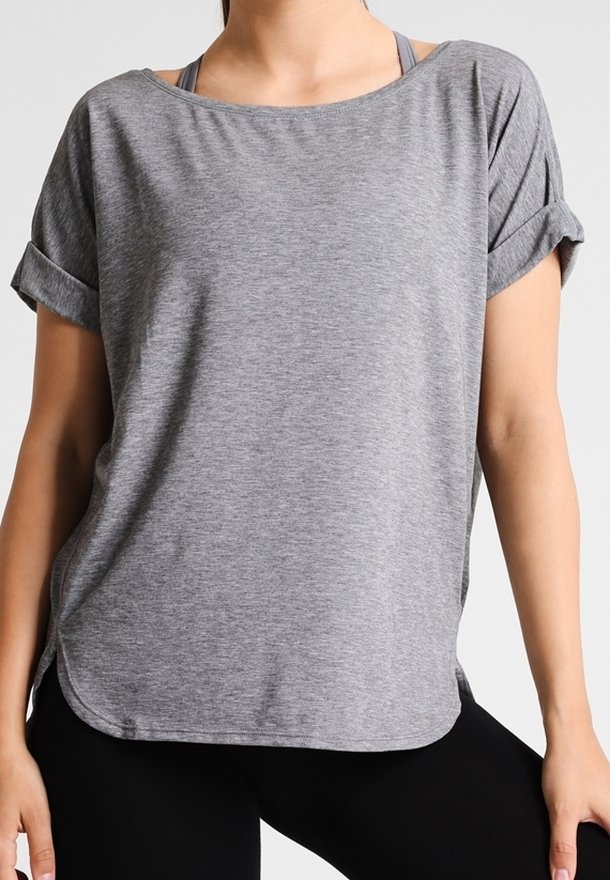 Grå t-shirt med korta ärmar och uppvikta cuffs, mjukt tyg, lös passform och rundad nederkant, lagd över en sport-bh.