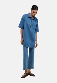 Tunique en denim à manches courtes, avec un col boutonné et une coupe droite, accompagnée de pantalons en denim à jambe large dans une teinte assortie.