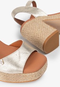 Sandalias de plataforma con una correa metálica dorada, base de yute trenzado y plantilla en tono beige. El diseño incluye un tacón moderado para mayor soporte.