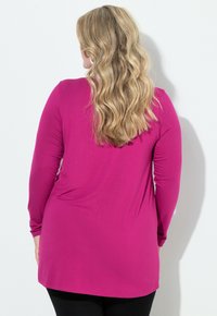 Maglietta a maniche lunghe di un vivace rosa, realizzata in tessuto morbido. Presenta una vestibilità ampia con orlo curvo, abbinata a leggings neri.