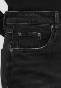 Mustad teksapüksid on tavapärase viie taskuga disainiga, metallist riistvara ja õmblustel ning taskutel kontrastset värvi niidiga.