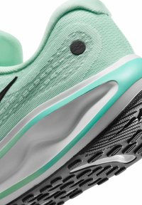 Scarpa da atletica verde chiaro con una tomaia testurizzata, dettagli neri, suola ammortizzata e battistrada in gomma con motivo per una migliore trazione.