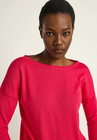Fuchsia sweater made of soft fabric with a relaxed fit, wide neckline, and long sleeves, featuring a smooth texture and minimal detailing.