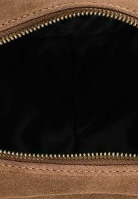 Tissu en daim marron avec une fermeture éclair dorée partiellement ouverte, montrant une doublure intérieure ou un compartiment noir.