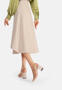 Gonna midi beige con un design fluido abbinata a sandali con tacco blocco nudo e ornamenti metallici, dotati di cinturini e dettagli testurizzati.