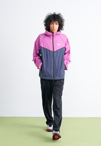 Nike hættetrøje i pink og navy med en frontlynlås, prydet med et chevron-design. Sammen med sorte træningsbukser og sneakers.