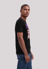 Black cotton t-shirt featuring a graphic print. Short sleeves, crew neck, relaxed fit, with a colorful design of a person on the front.