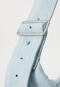 Svetlo modra denim zanka z zlatim kovinskim sponko, vidnimi šivi in več luknjami za prilagoditev. Gladka tekstura.