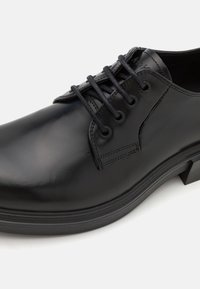Black leather dress shoe with round toe, five eyelet lacing, smooth finish, and a low-profile rubber sole. Subtle stitching detail on the upper.