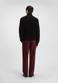 Schwarzer, strukturierter Pullover mit hohem Kragen und geripptem Saum, kombiniert mit burgunderroten, locker sitzenden Hosen und schwarzen Schuhen.