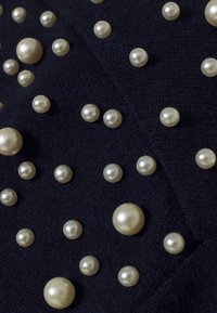 Granatowa tkanina z rozproszonymi kremowymi sztucznymi perłami w różnych rozmiarach, z fakturowanym tłem z dzianiny.